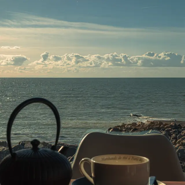A cup of tea and a teapot on a table near the sea