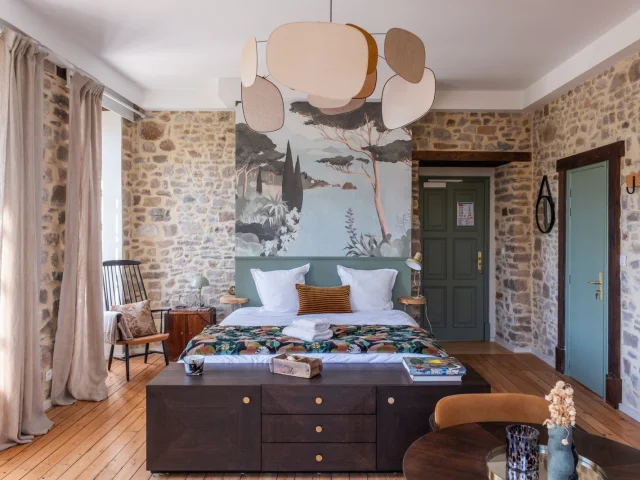 Chambre avec lit, tête de lit décorative, et murs en pierre apparente : éco domaine du Plessis